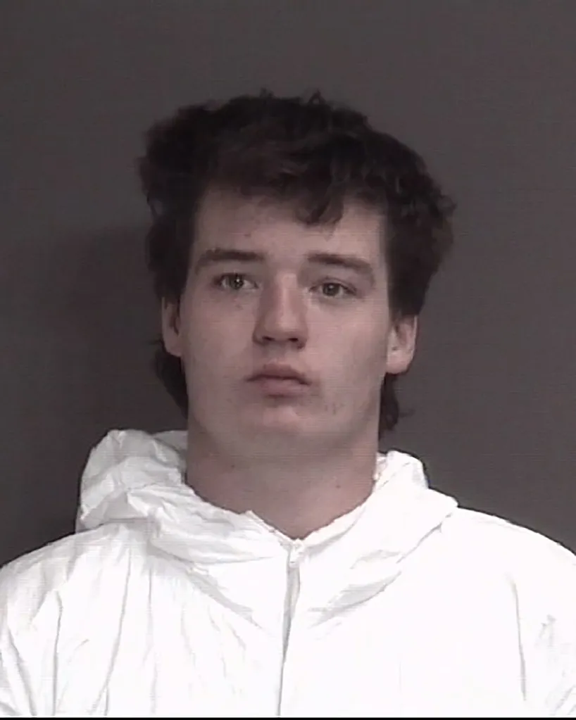 Mugshot of a young man with dark, messy hair and a white hooded garment.