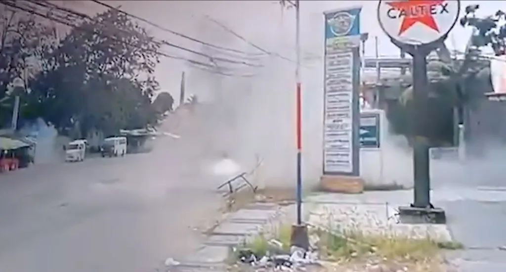 Smoke rising from the side of a road, with two white vans in the background and a Caltex sign visible on the right.
