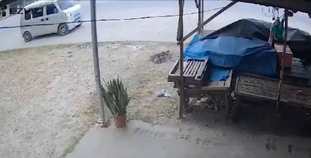 A white van drives past a roadside stand with blue tarps.