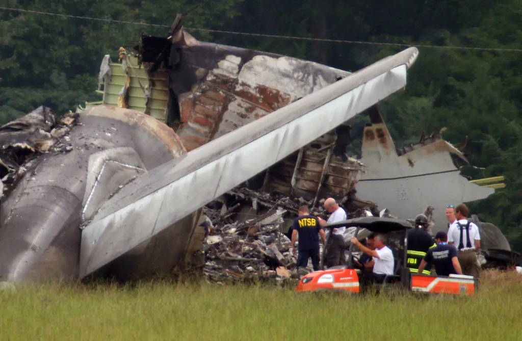 NTSB investigators examine the tail section of a crashed UPS cargo plane in a grassy field.
