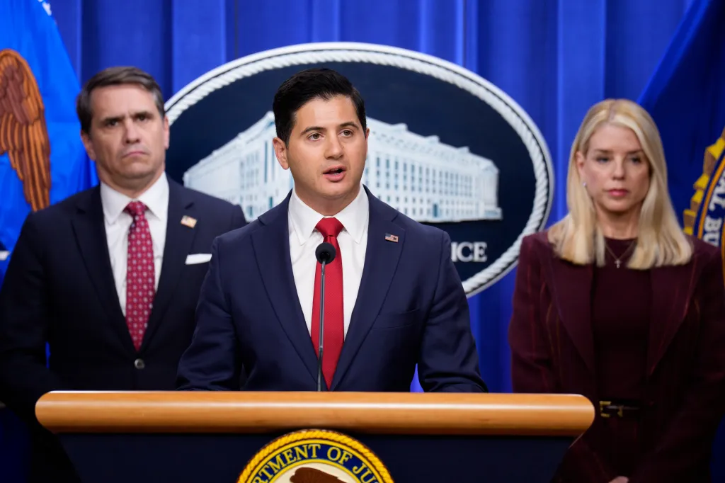 First Assistant U.S. Attorney Bill Essayli speaking at a news conference, flanked by Attorney General Pam Bondi and Deputy Attorney General Todd Blanche.