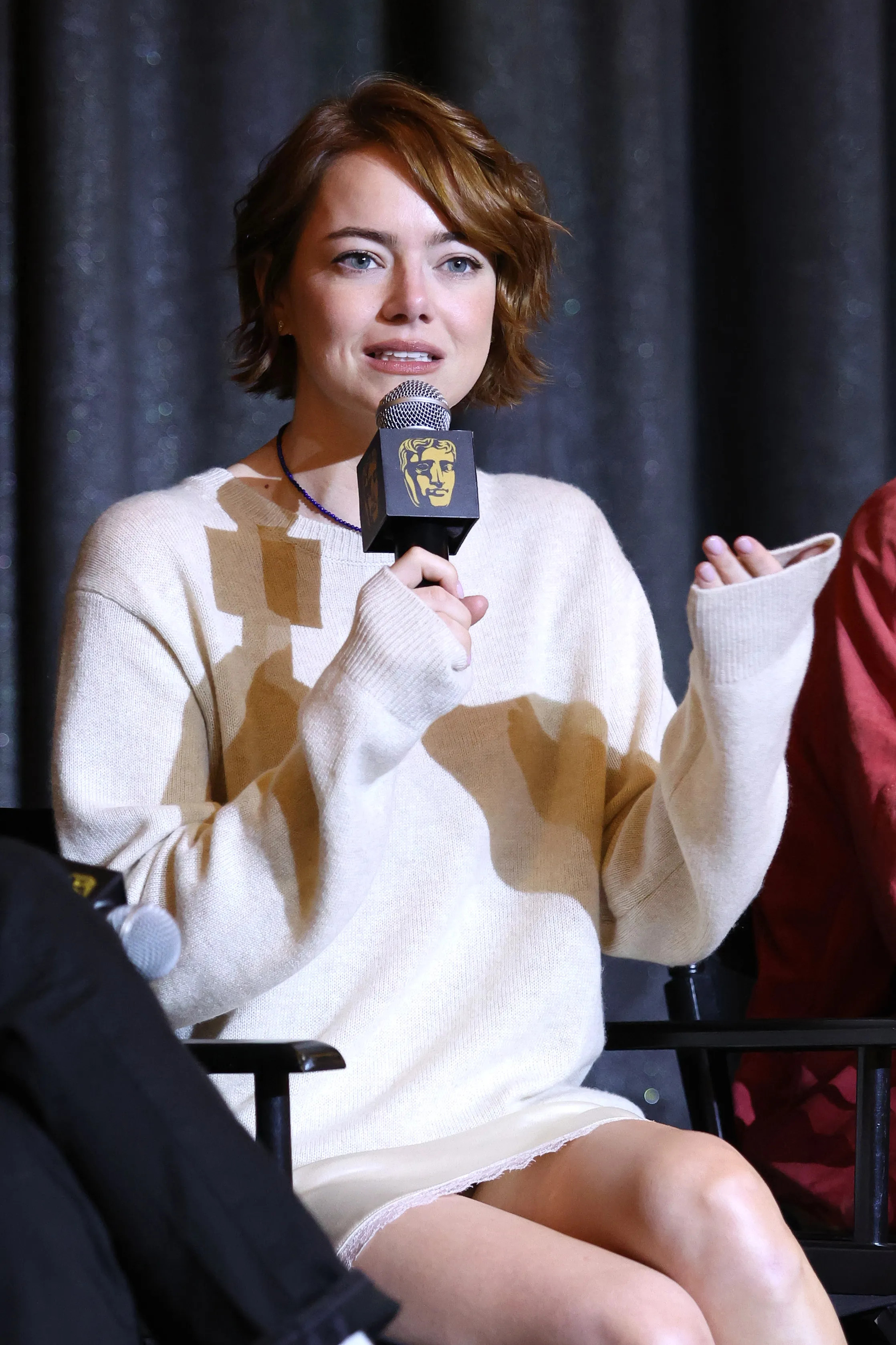 Emma Stone speaks onstage with a BAFTA-branded microphone at the 