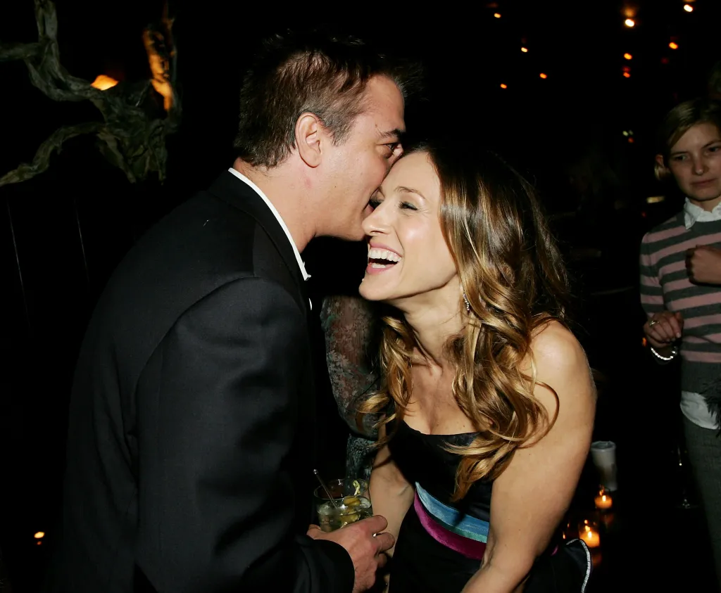 Actor Chris Noth kisses actress Sarah Jessica Parker on the forehead as she laughs, holding a drink.