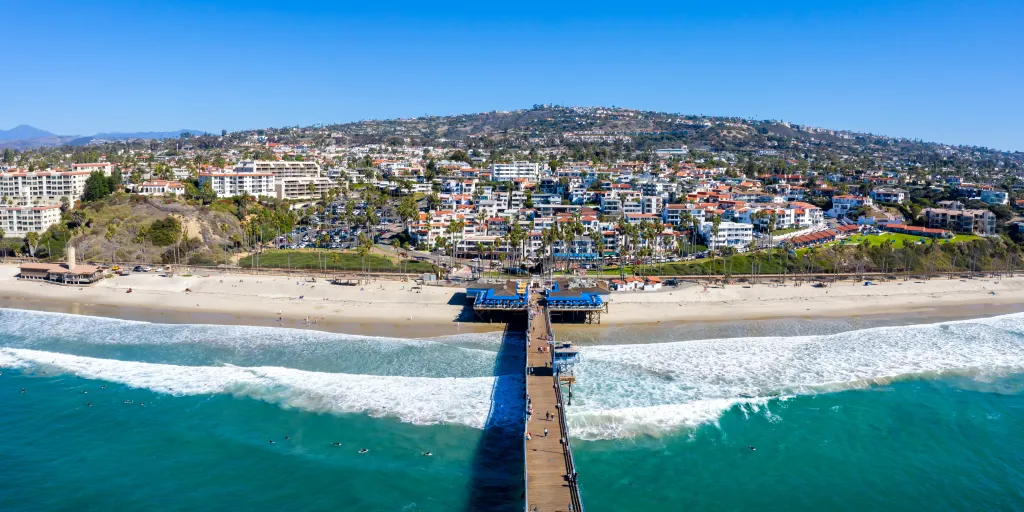 Aerial view of San Clemente, California, with a pier extending into the Pacific Ocean, a beach, and a hillside town.