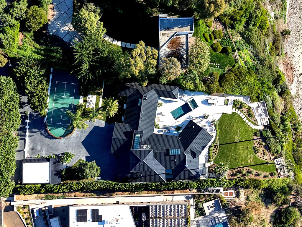 Aerial view of Sergey Brin's clifftop property in Malibu, featuring a house with dark roofs, swimming pools, a tennis court, and extensive green landscaping.