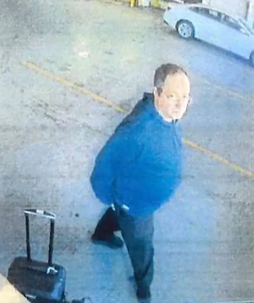 Surveillance photo of Claudio Neves Valente in a blue top and dark pants, with a suitcase, and a light-colored car in the background.