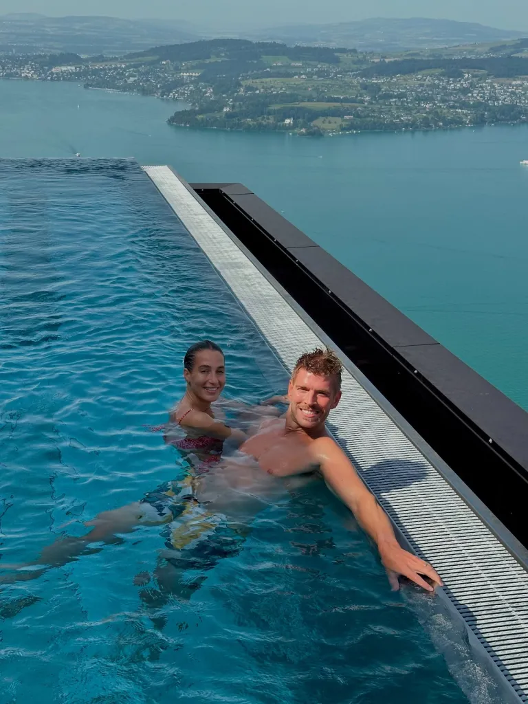 Amanda Batula and Kyle Cooke in an infinity pool overlooking a lake and town.