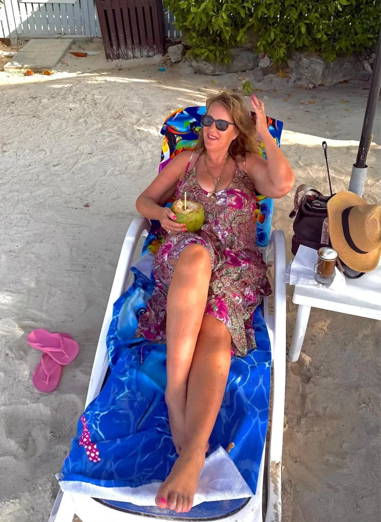 A woman on a beach in a lounge chair holding a coconut drink.