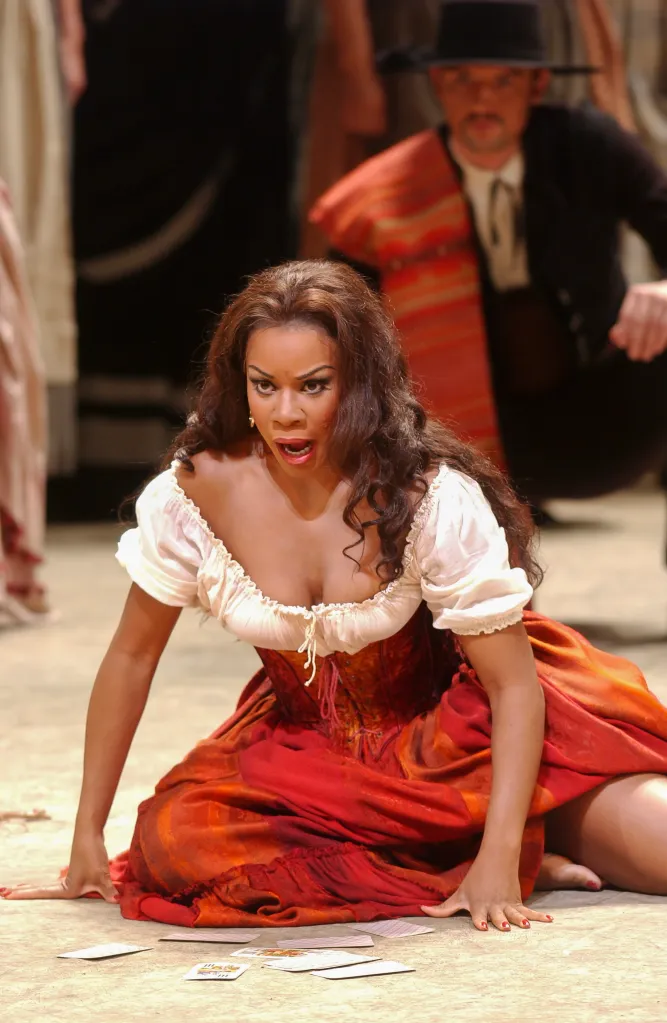 Denyce Graves performs as Carmen, kneeling with tarot cards spread on the floor, in a white ruffled peasant blouse and a red and orange skirt.