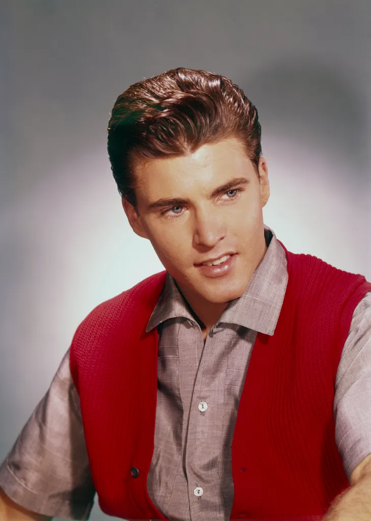 Portrait of Ricky Nelson wearing a red waistcoat over a grey shirt.