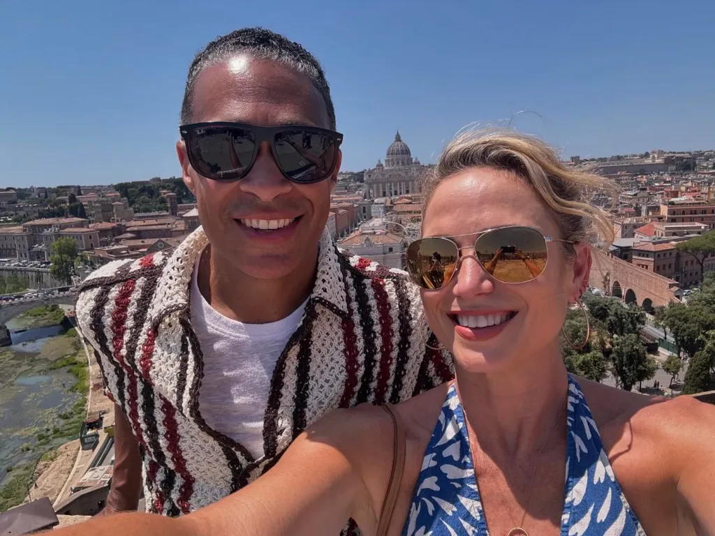 Amy Robach and T.J. Holmes smiling with a city skyline in the background.