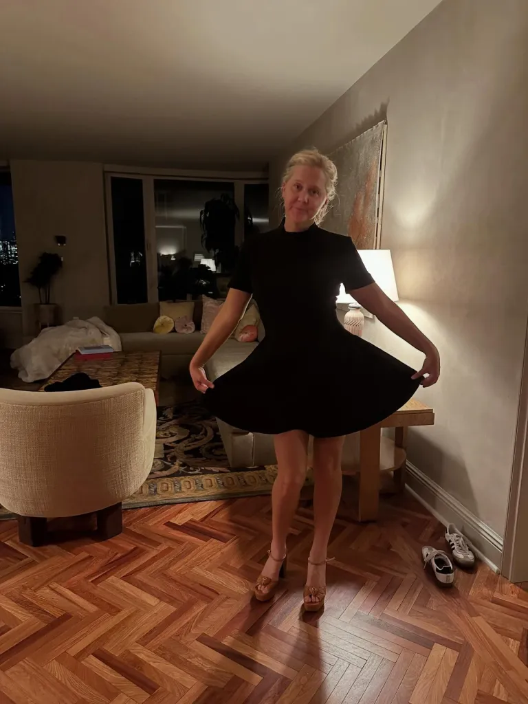 Amy Schumer in a black dress in a living room.