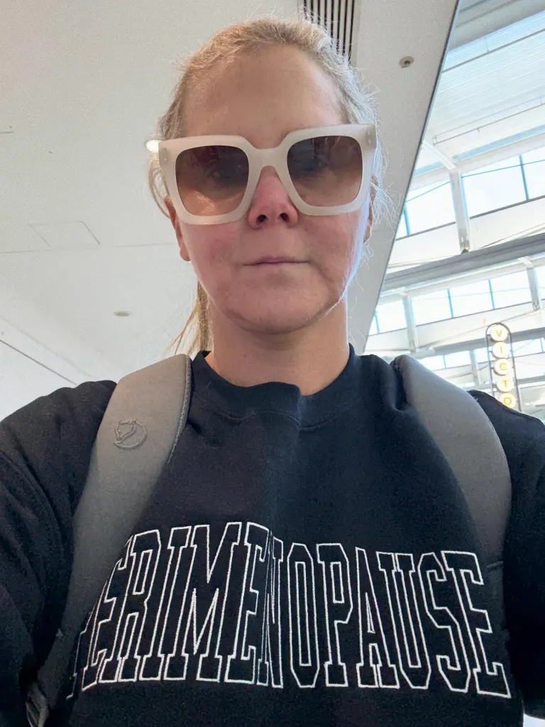 Amy Schumer wearing sunglasses and a black sweatshirt that says