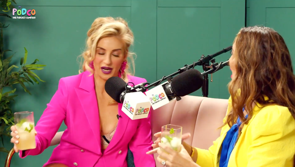 Annaliese Van Der Pol and an interviewer, seated and holding drinks, talking into microphones.