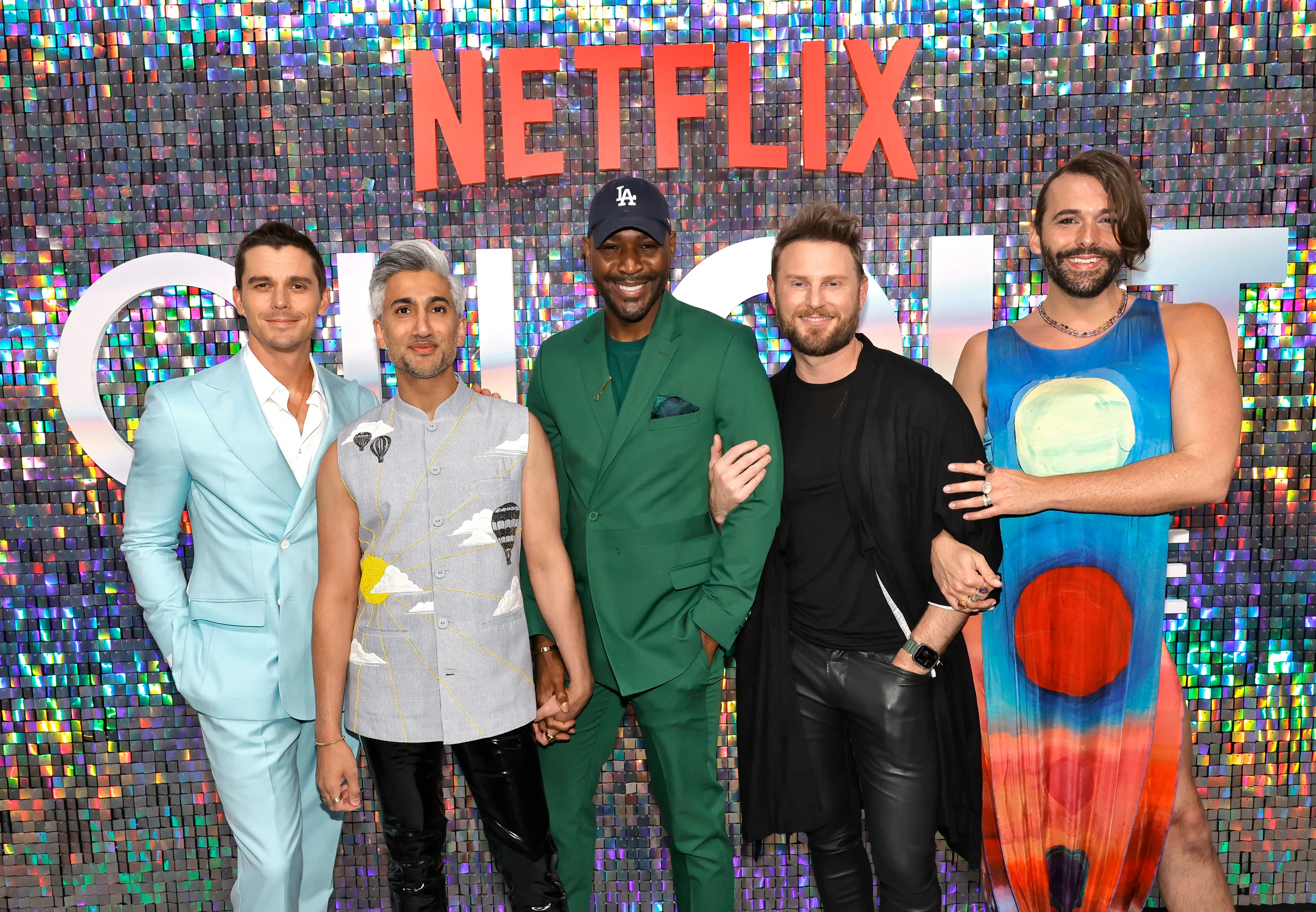 The cast of Queer Eye, Antoni Porowski, Tan France, Karamo Brown, Bobby Berk, and Jonathan Van Ness, posing in front of a Netflix sign at a Pride event.