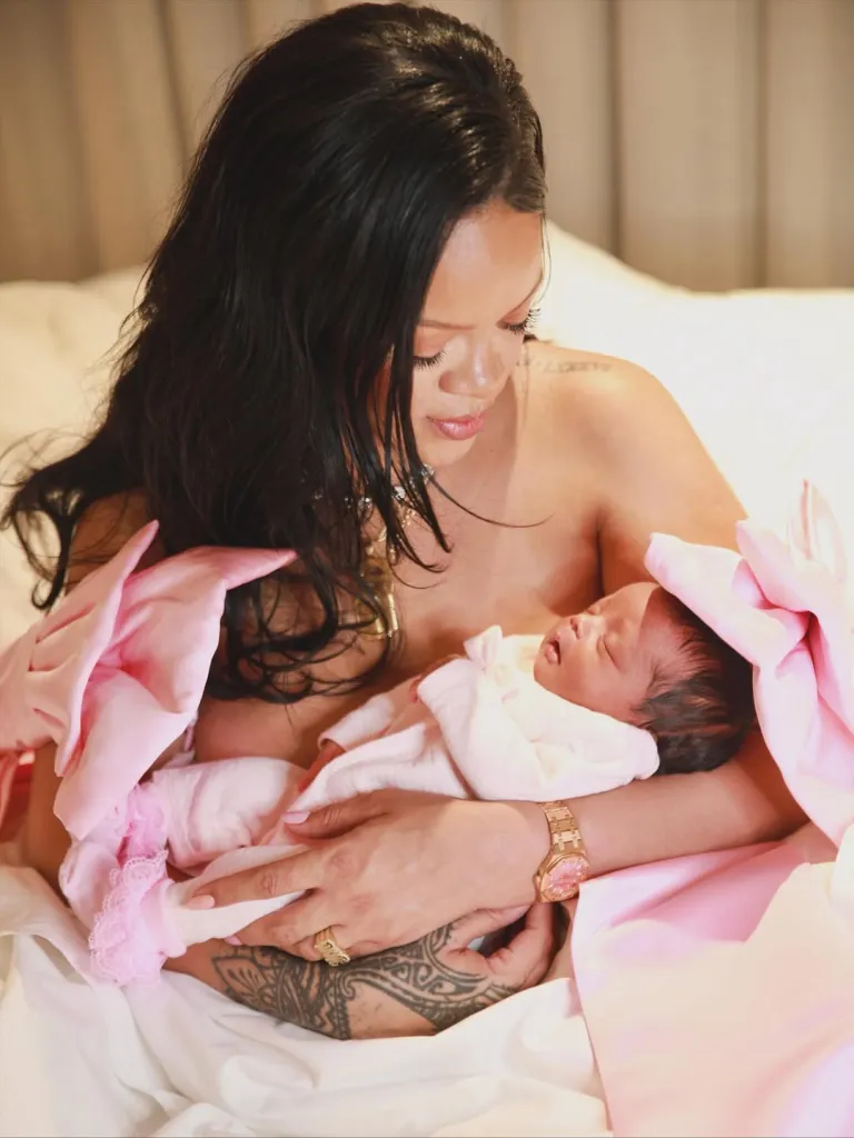 Rihanna holding her newborn baby, who is swaddled in pink.