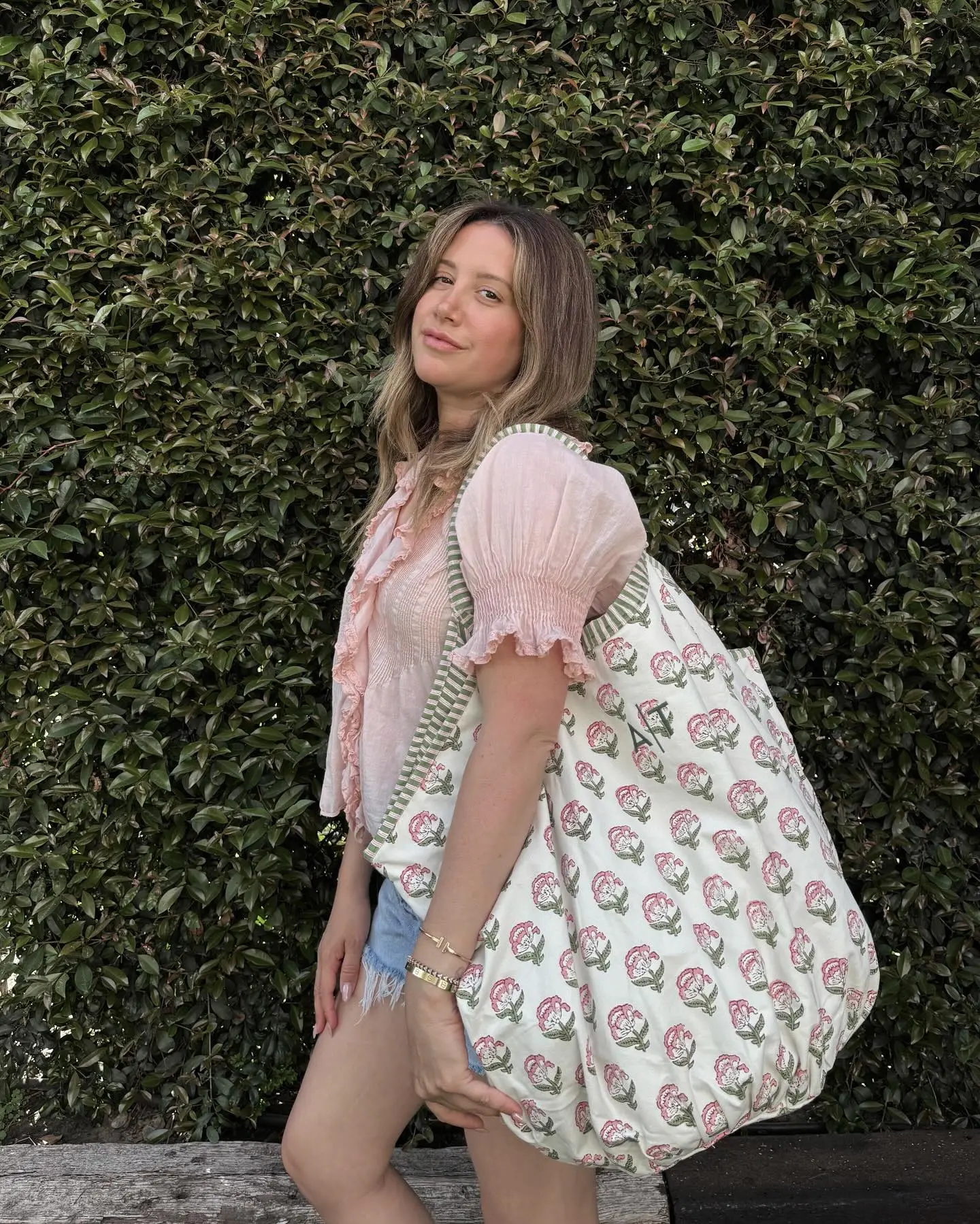 Ashley Tisdale posing with a large tote bag with pink floral patterns.