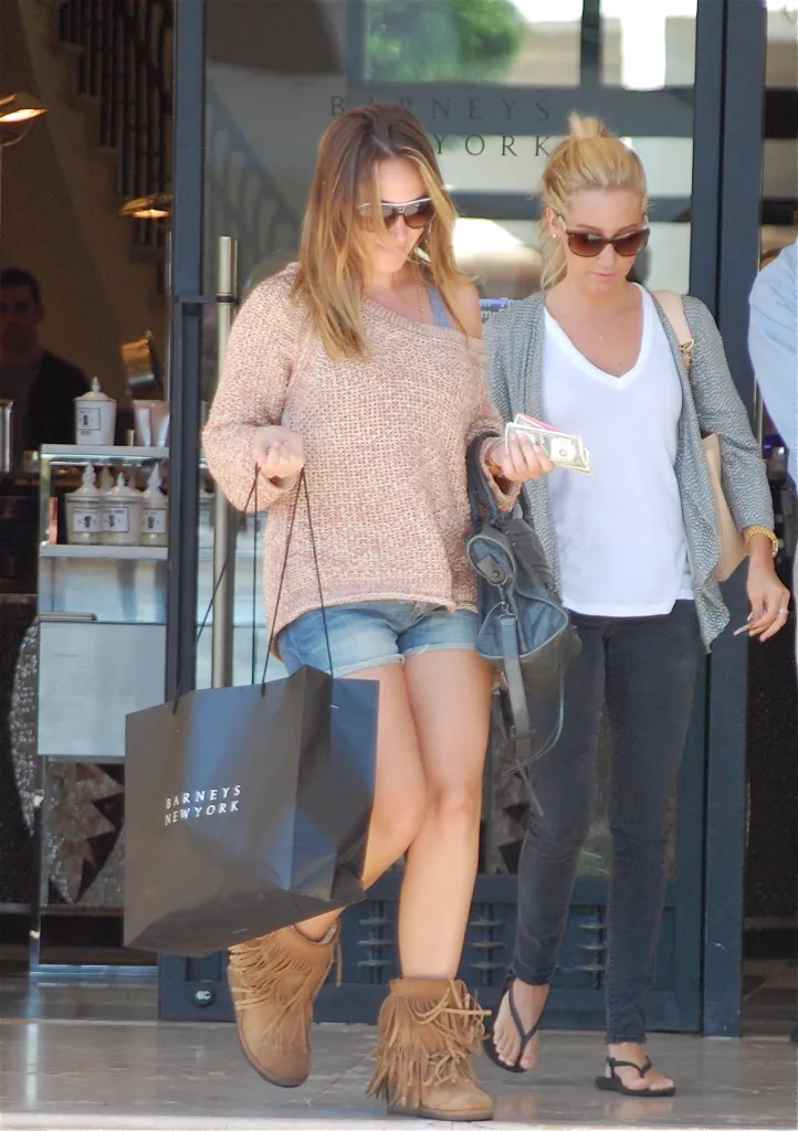 Haylie Duff exits Barneys New York carrying a shopping bag, while Ashley Tisdale walks beside her holding cash.