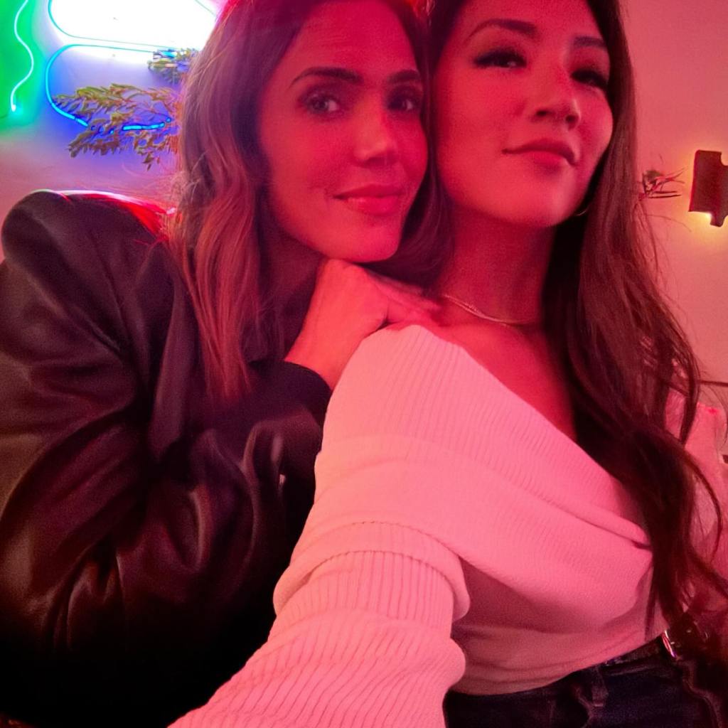 Mandy Moore and her friend posing for a selfie in pink lighting.
