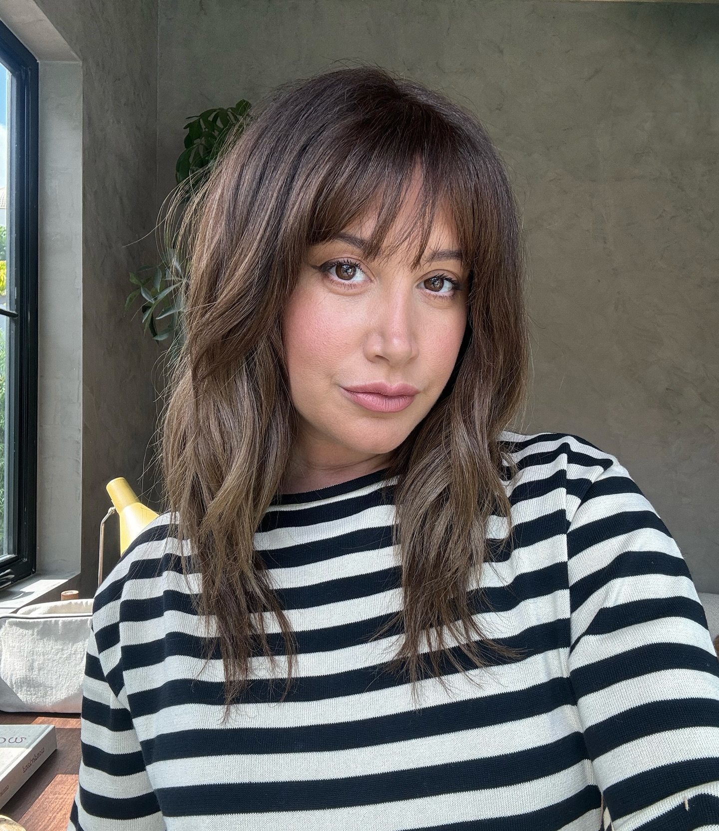 Ashley Tisdale looking at the camera, wearing a black and white striped shirt.