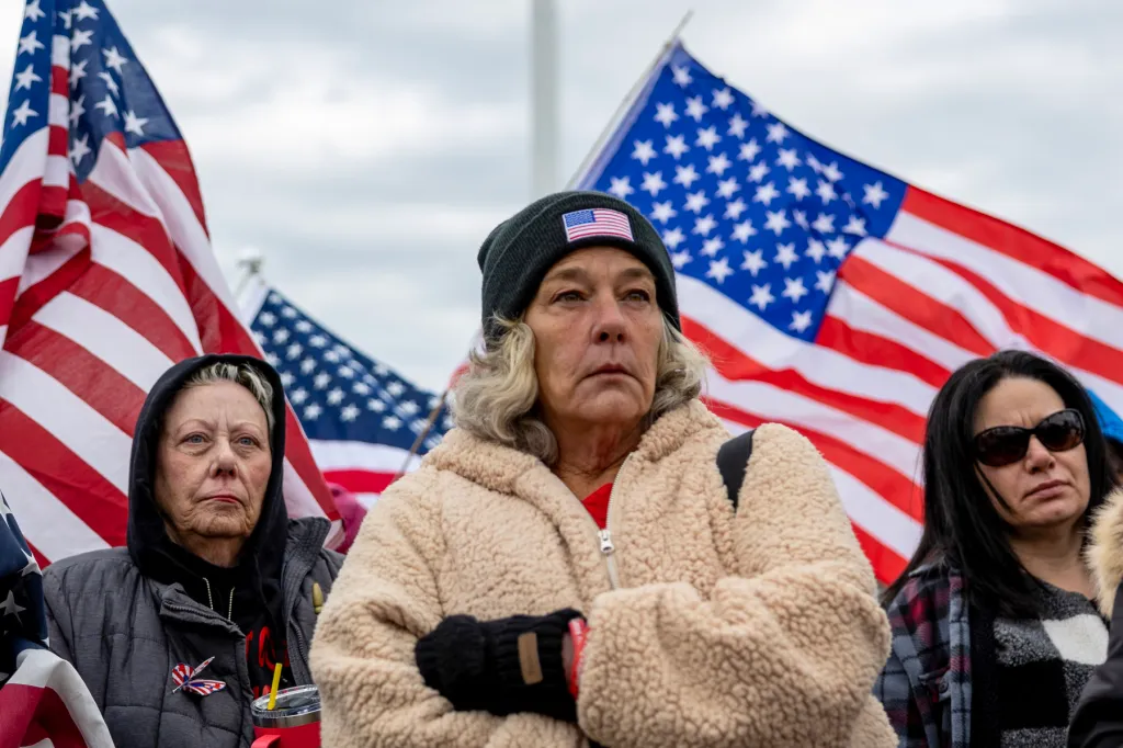 Witthoeft frowns with arms crossed in front of large American flags, surrounded by other women.