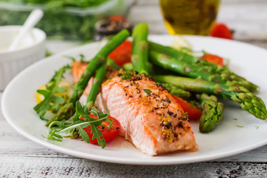 Baked salmon fillet garnished with asparagus, cherry tomatoes, and herbs on a white plate.