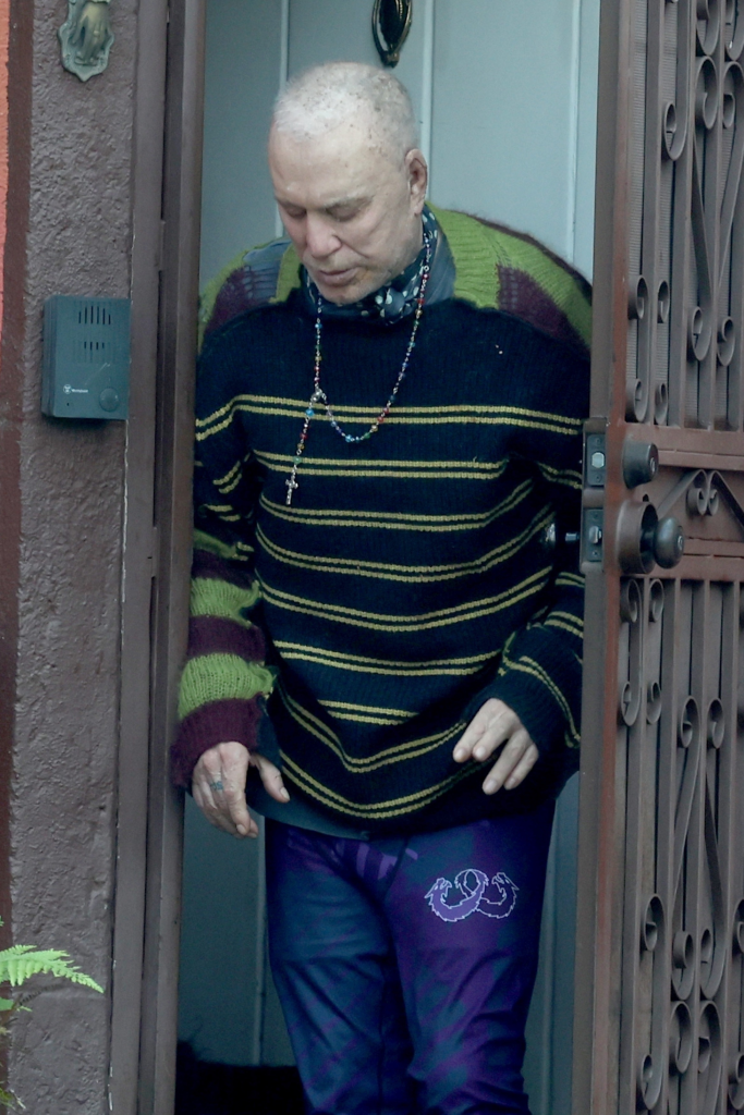 Bald Mickey Rourke looking down while exiting a doorway.
