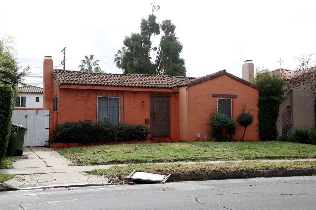 A single-story orange house with a tile roof and overgrown yard.