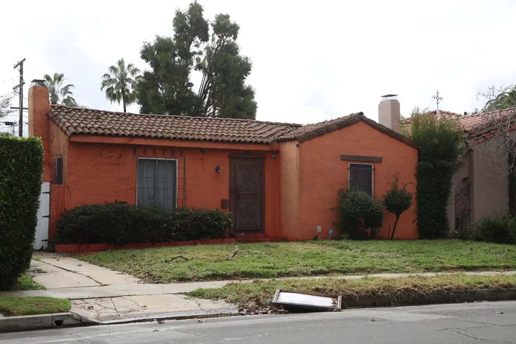A burnt orange house with a tiled roof, surrounded by overgrown landscaping.