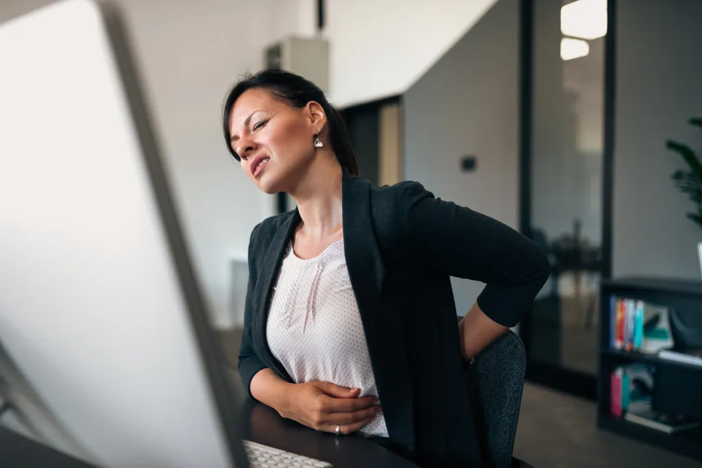 Young businesswoman experiencing back pain while sitting at her office desk.