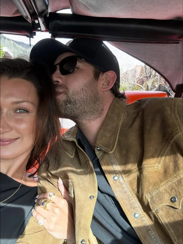 Bella Hadid and Adan Banuelos in a car, Hadid smiling and wearing rings, Banuelos in a baseball cap and sunglasses.