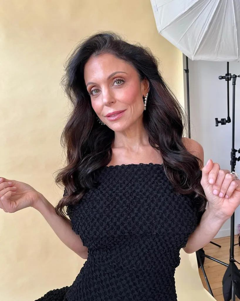 Bethenny Frankel, wearing a black off-the-shoulder dress with textured fabric, poses for a photo.