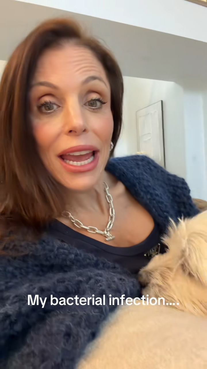 Bethenny Frankel, wearing a dark blue sweater and a silver chain necklace, speaks to the camera while holding a light-colored dog.