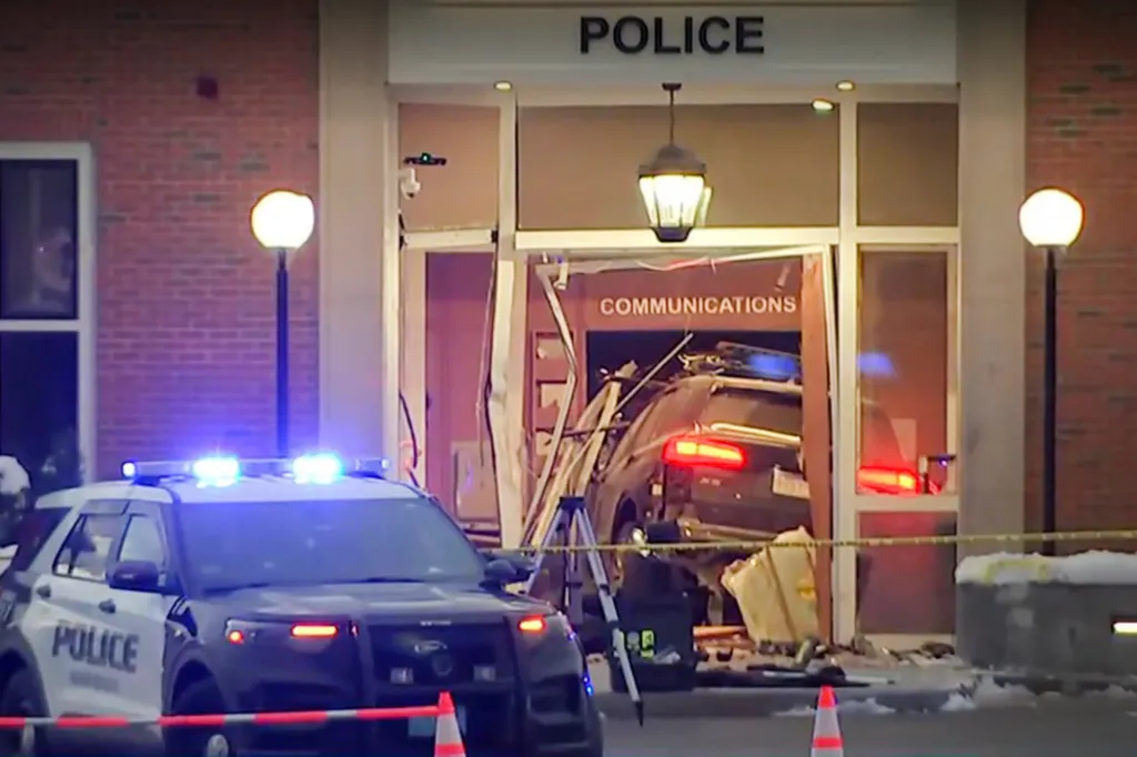 A black SUV crashed into a police station, with a police car and caution tape in the foreground.