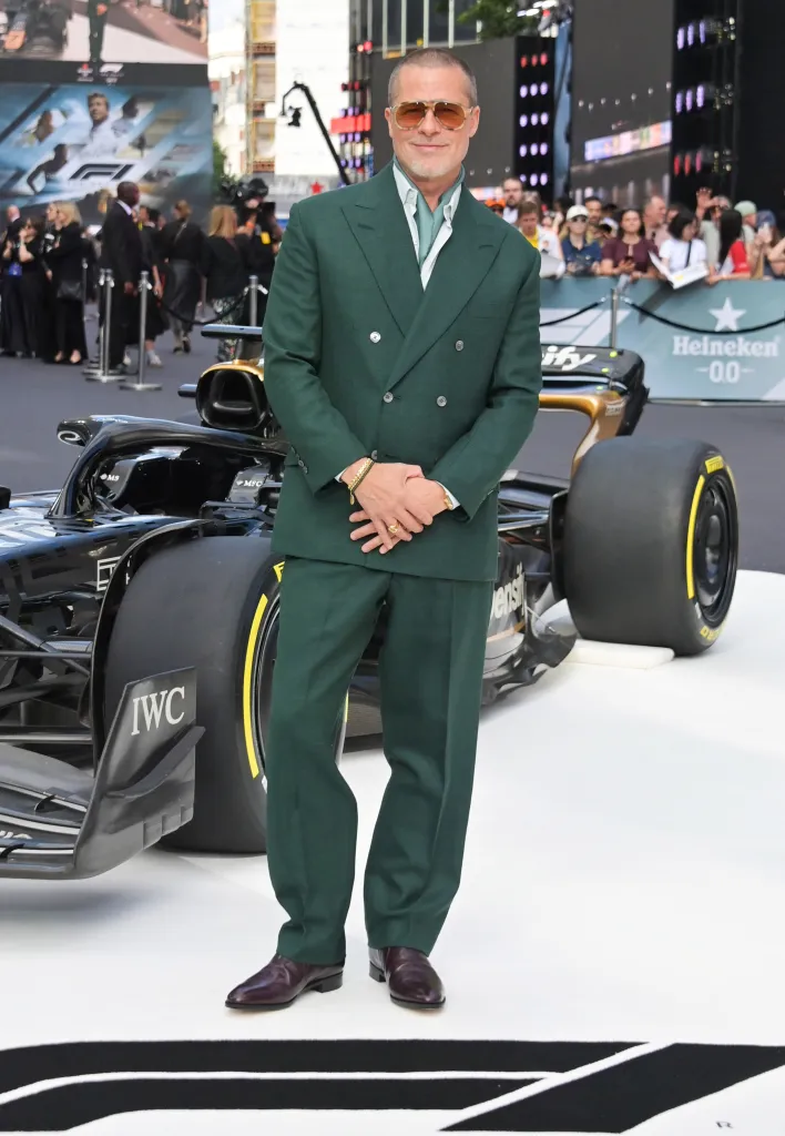 Brad Pitt wearing a green suit and sunglasses, standing next to a Formula 1 car at a movie premiere.