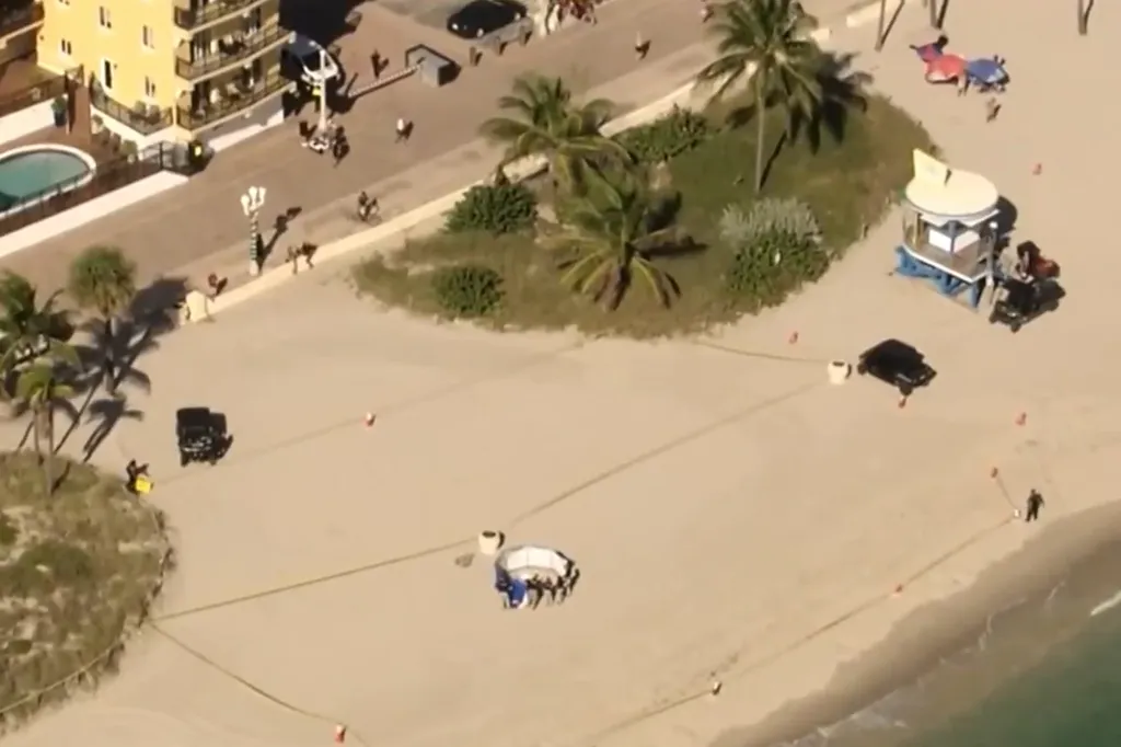 Aerial view of the Hollywood, Florida beach crime scene where Heather Asendorf's body was discovered, showing a section of the beach cordoned off with tape and several police vehicles present.