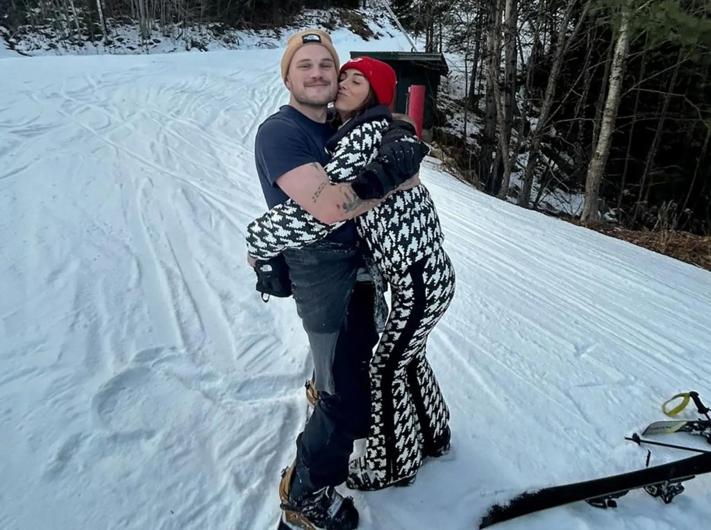 Brianna Chickenfry and Zach Bryan embrace on a snowy slope.
