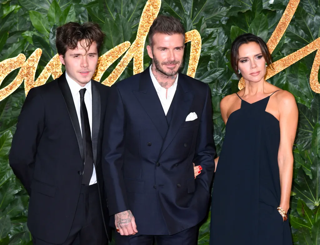 Brooklyn Beckham, David Beckham, and Victoria Beckham pose on a red carpet.