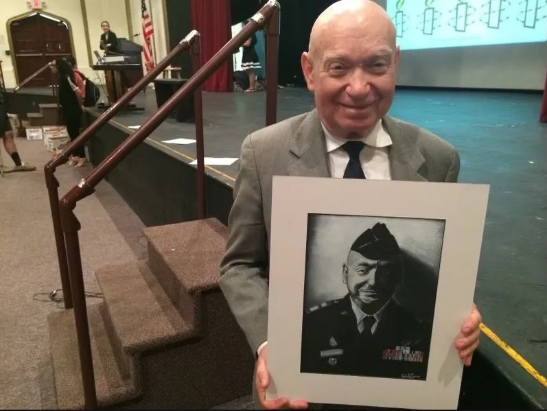 Sami Steigmann, a Holocaust survivor, holding a framed portrait of himself in military uniform.