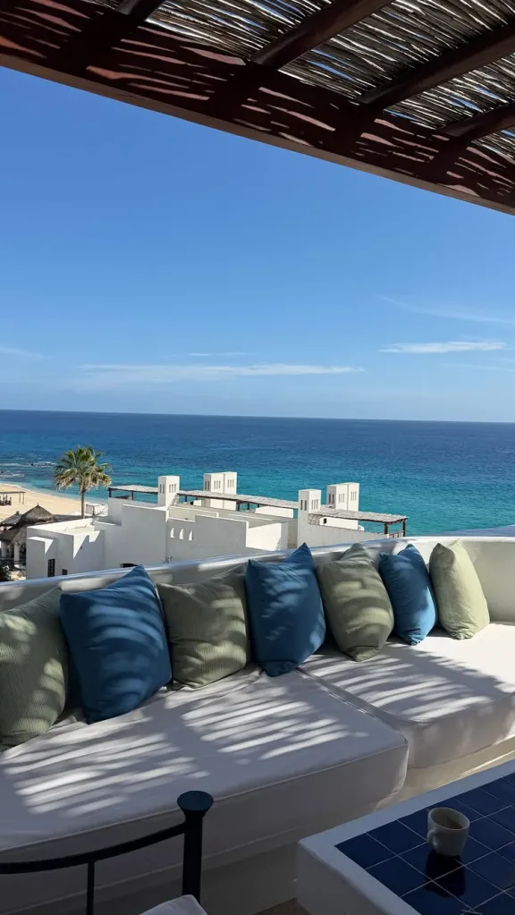 A scenic view of the ocean and beach from a balcony with a couch and pillows.