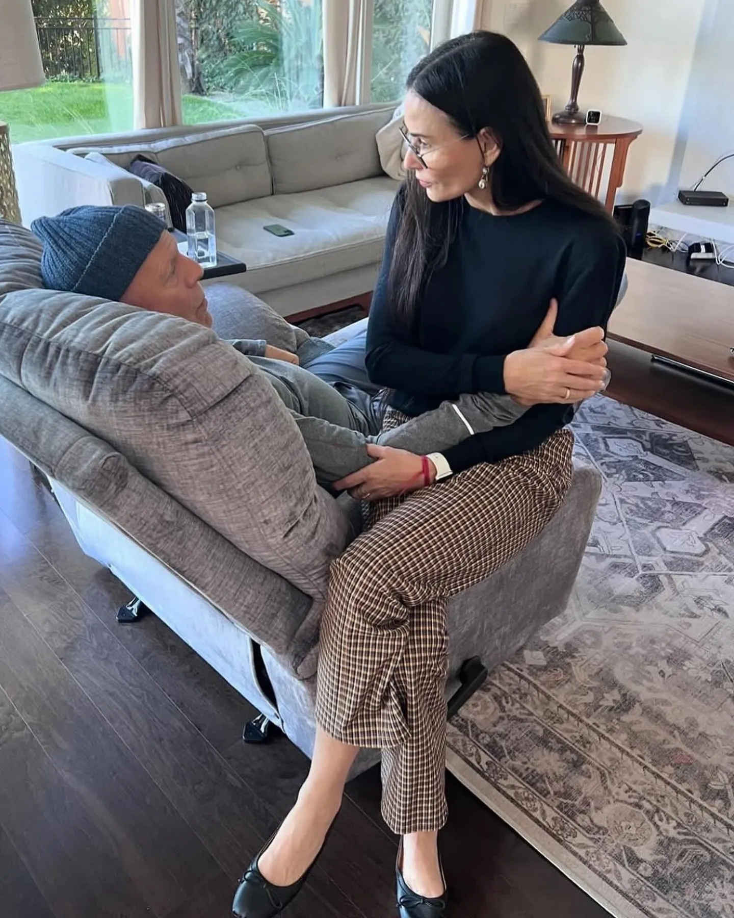 Demi Moore seated on a chair armrest, holding hands with Bruce Willis who is resting in an adjacent chair.