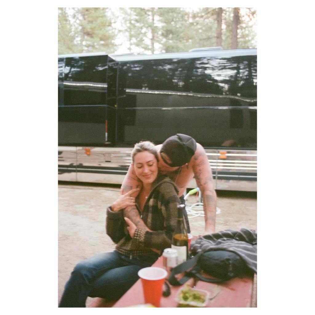 Zach Bryan kissing Samantha Leonard while she is seated at a table.