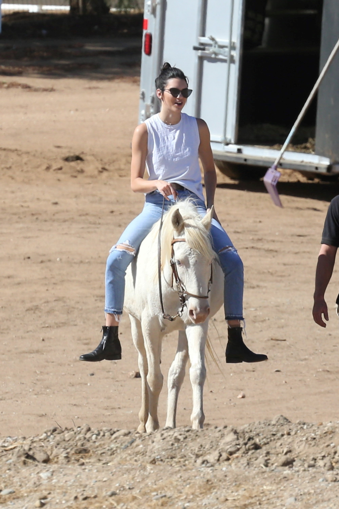 Kendall Jenner riding a white horse in ripped jeans and a white tank top.