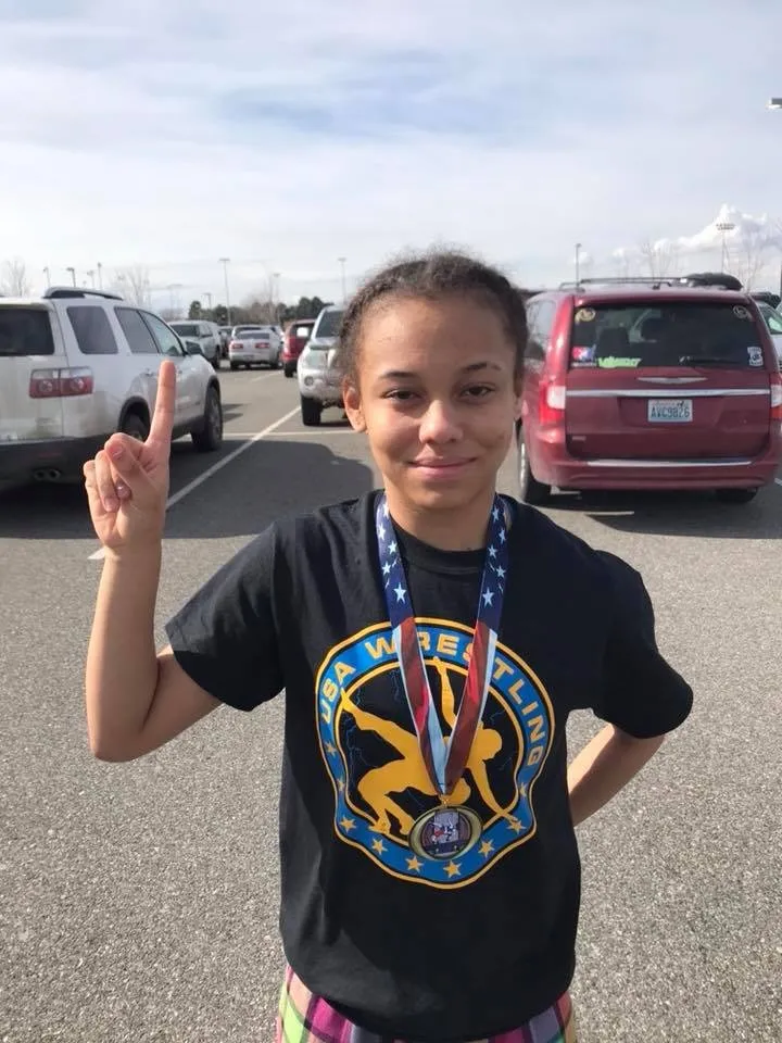 Carmen Anita Degregg wearing a USA wrestling shirt and medal, holding up one finger.