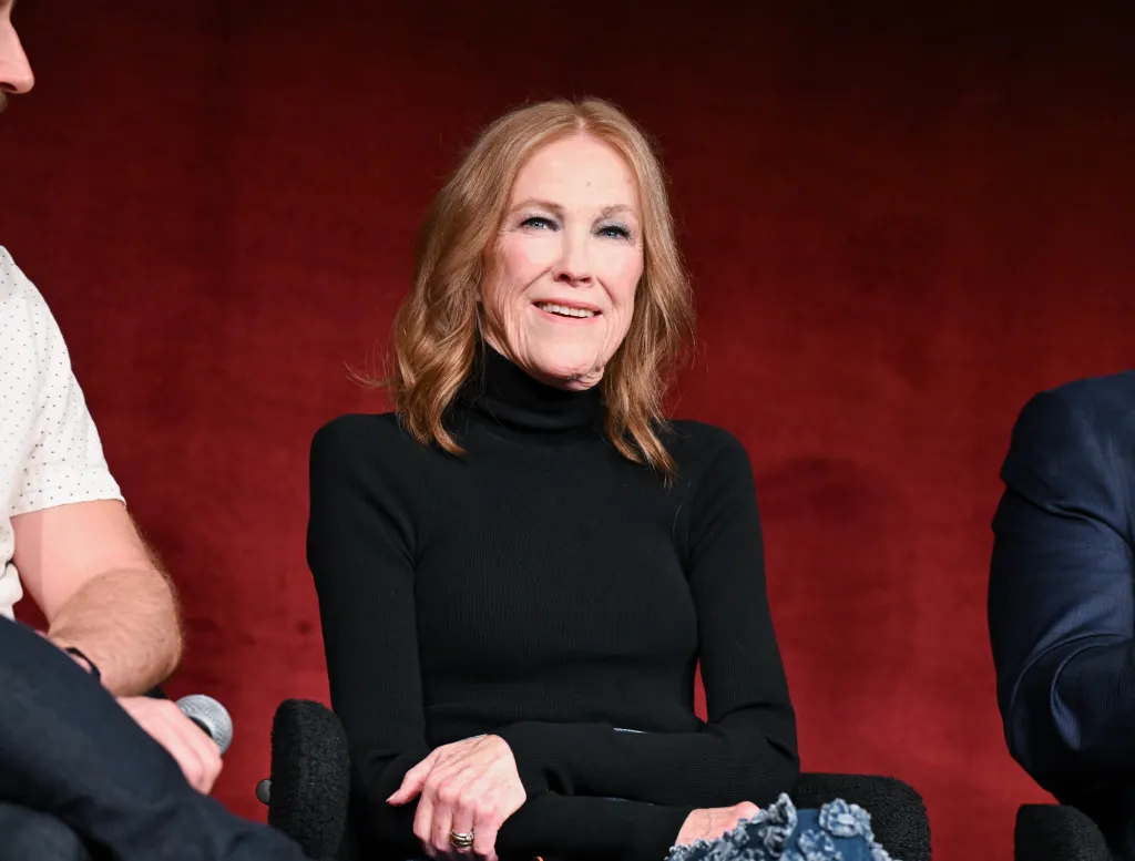 Catherine O'Hara smiles while wearing a black turtleneck.
