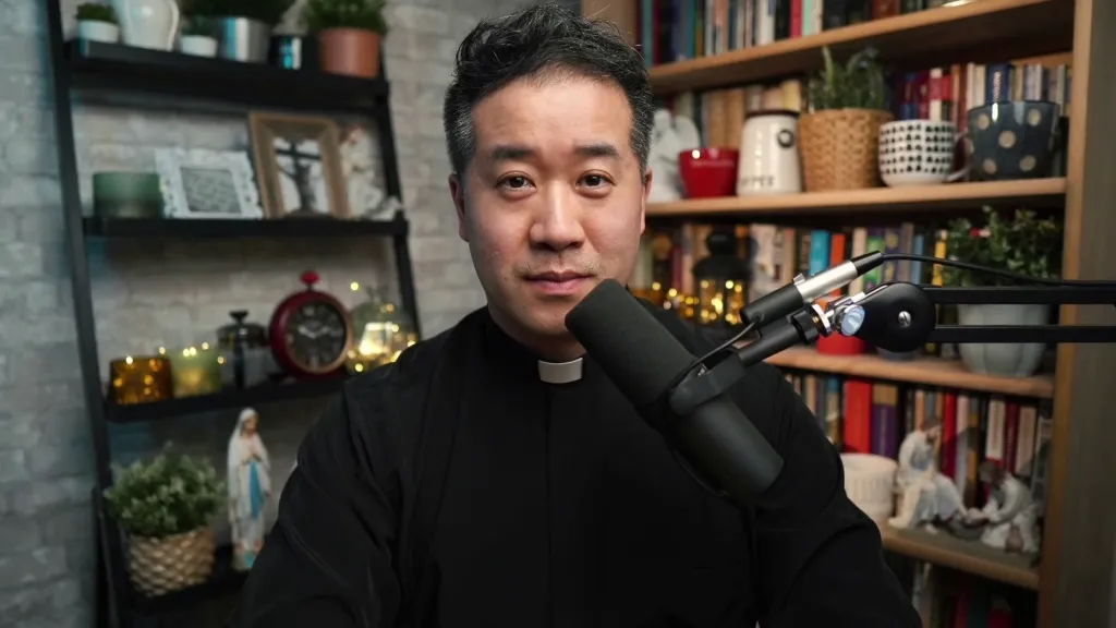 Father Eric Mah, a Catholic priest, sitting in front of a microphone and bookcase.