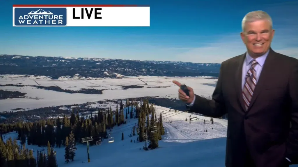 CBS 2 Chief Meteorologist Roland Steadham reporting live from a snowy mountain with ski lifts and distant frozen lakes and mountains.