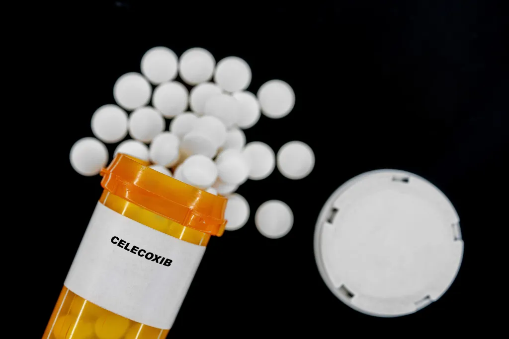 Celecoxib pills spilling from an orange prescription bottle.