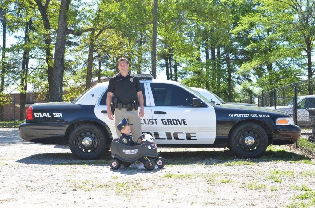 Chase Maddox standing with a child in a toy police car.