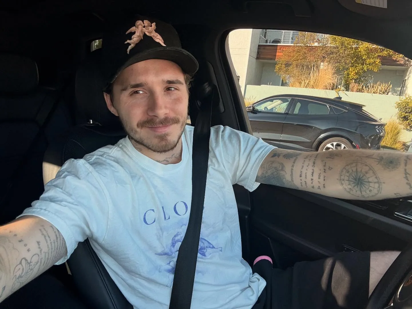 Brooklyn Beckham posing in a white t-shirt and a black baseball cap.